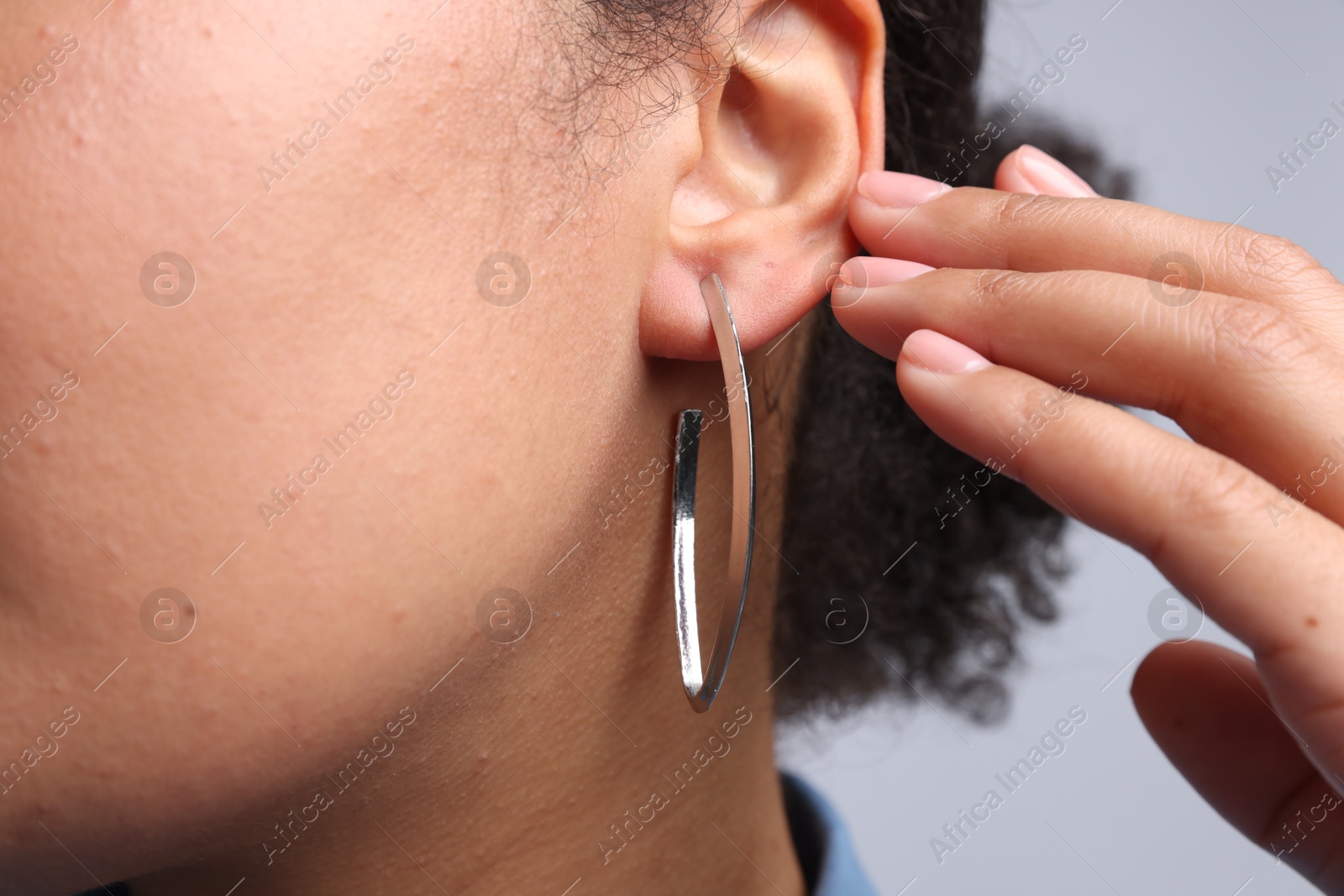 Photo of Young woman wearing elegant silver earring on light grey background, closeup