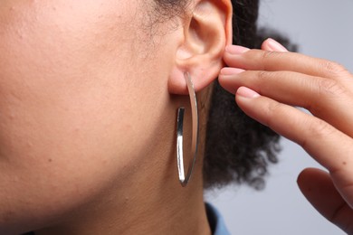 Photo of Young woman wearing elegant silver earring on light grey background, closeup