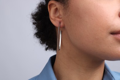 Photo of Young woman wearing elegant silver earring on light grey background, closeup. Space for text