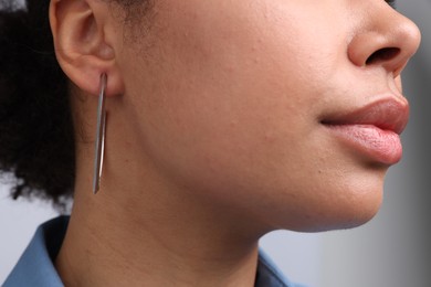 Photo of Young woman wearing elegant silver earring on light grey background, closeup