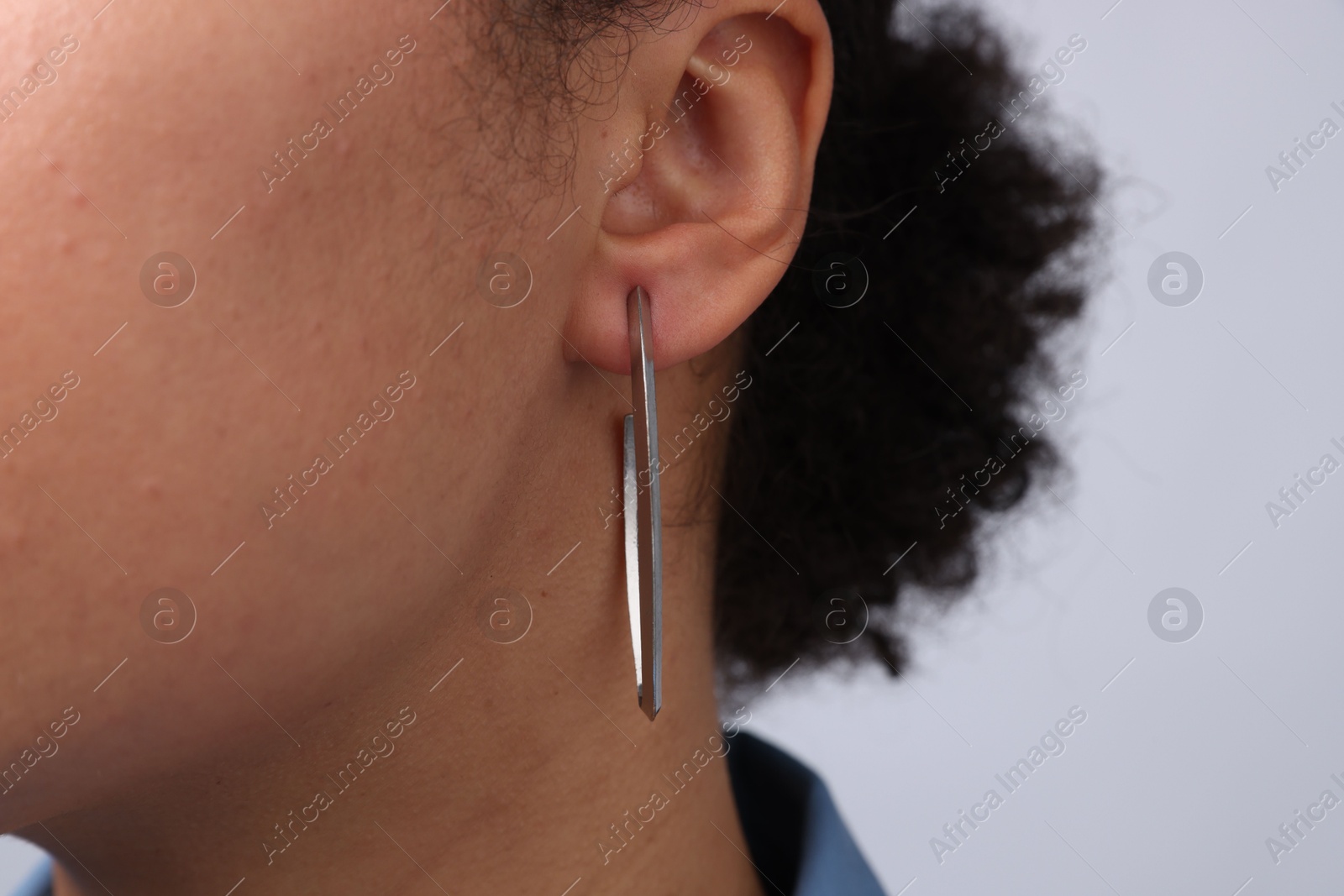 Photo of Young woman wearing elegant silver earring on light grey background, closeup