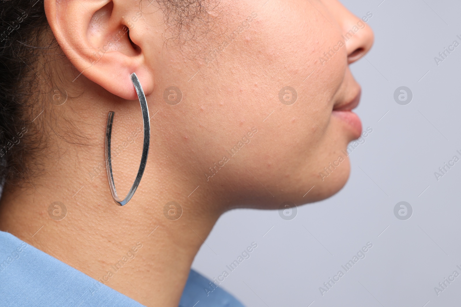 Photo of Young woman wearing elegant silver earring on light grey background, closeup