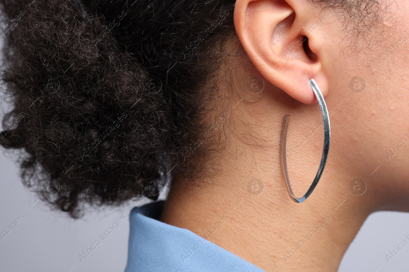 Photo of Young woman wearing elegant silver earring on light grey background, closeup
