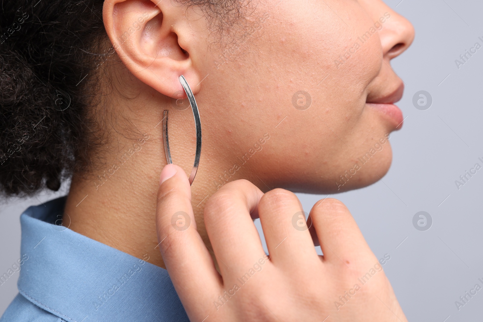 Photo of Young woman wearing elegant silver earring on light grey background, closeup