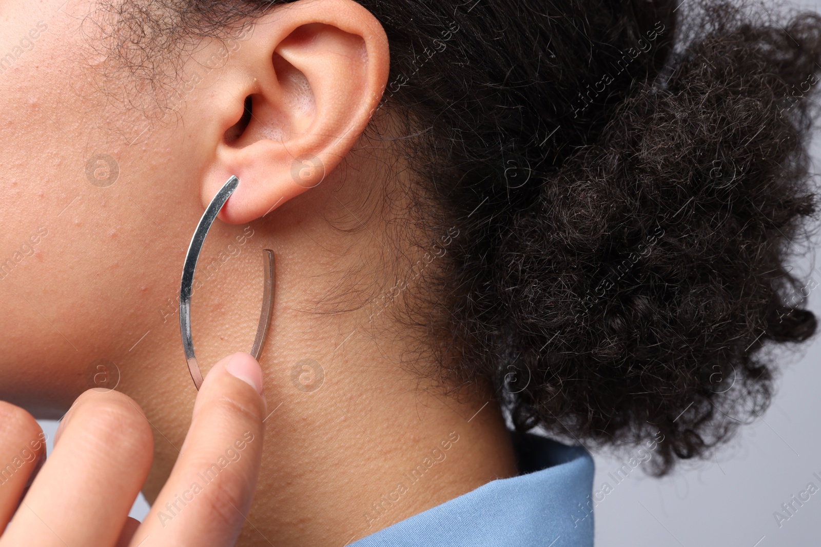 Photo of Young woman wearing elegant silver earring on light grey background, closeup