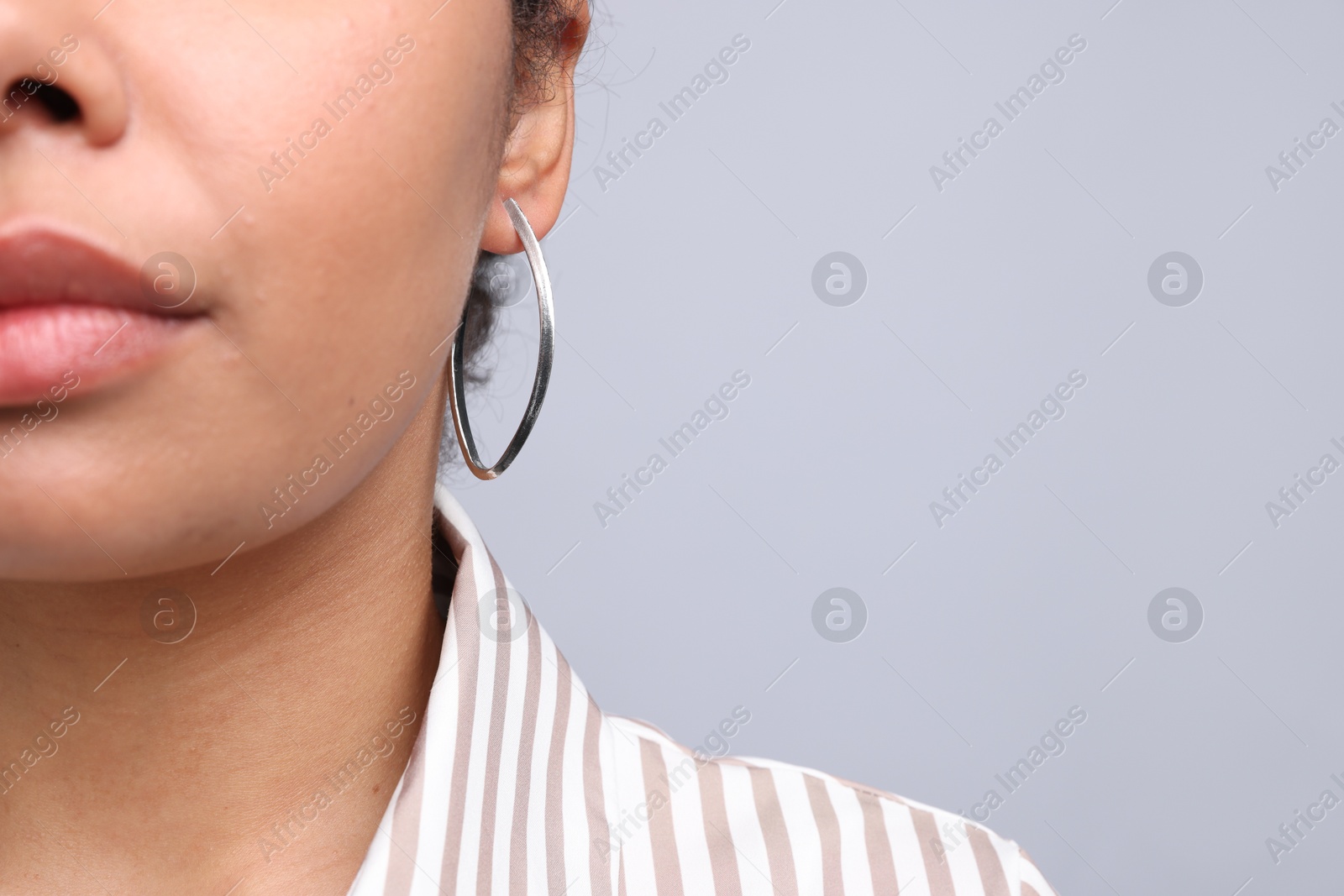 Photo of Young woman wearing elegant silver earring on light grey background, closeup. Space for text
