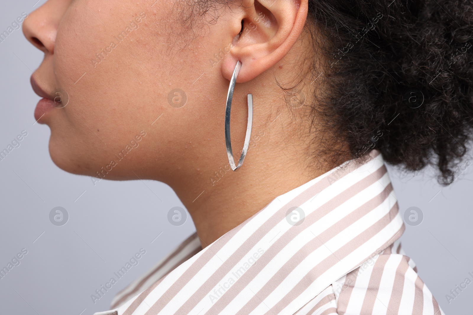 Photo of Young woman wearing elegant silver earring on light grey background, closeup