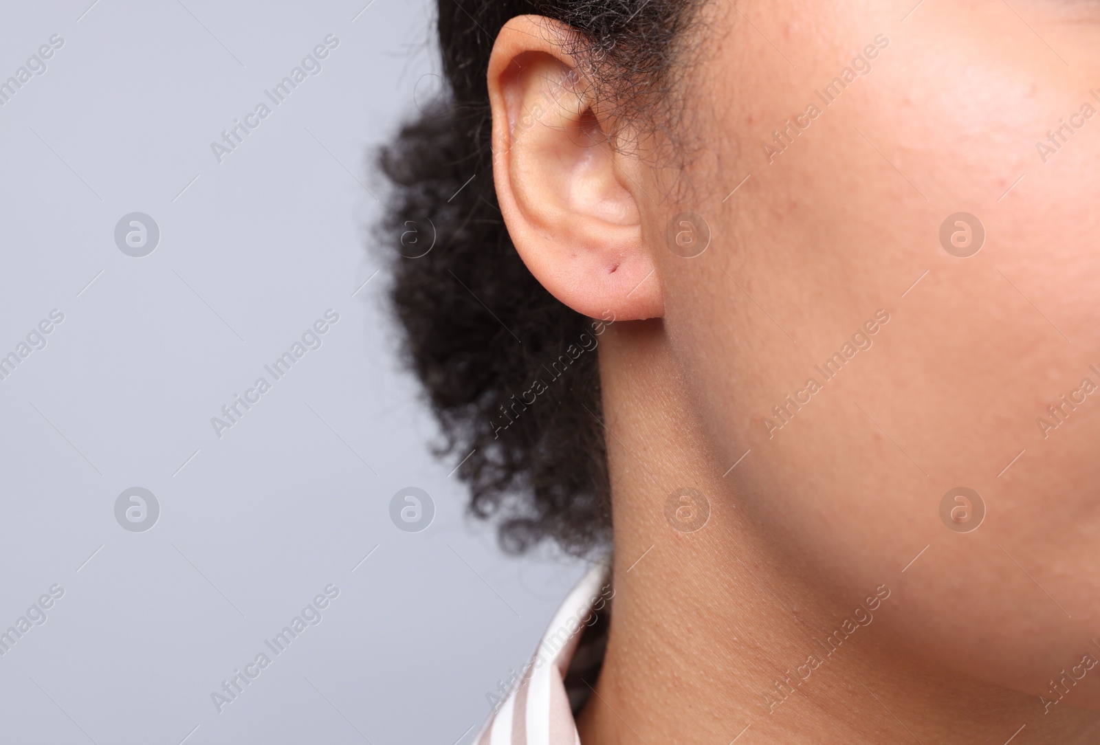 Young woman with pierced ear on light grey background, closeup. Space for text Photo of Young woman with pierced ear on light grey background, closeup. Space for text