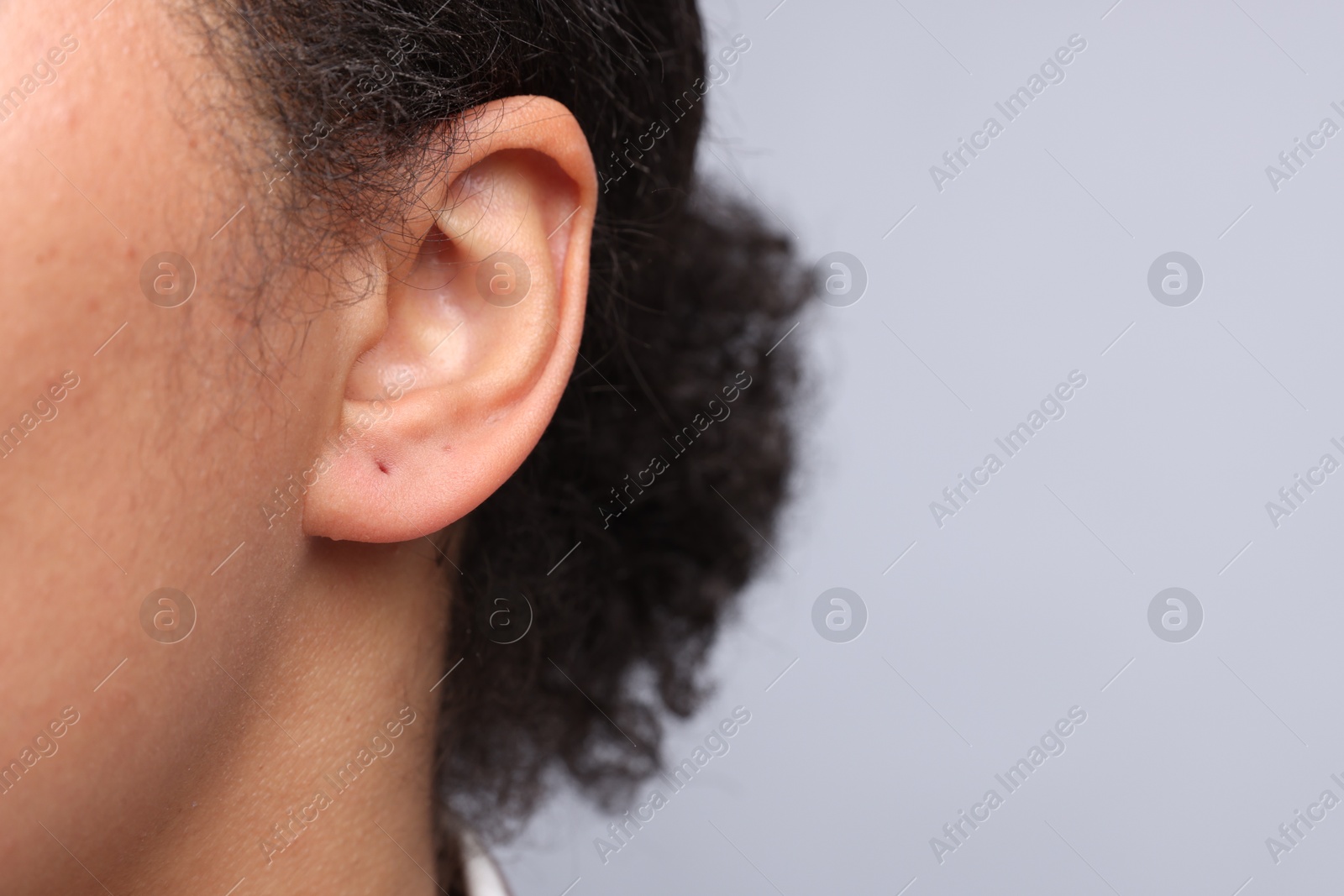 Young woman with pierced ear on light grey background, closeup. Space for text Photo of Young woman with pierced ear on light grey background, closeup. Space for text