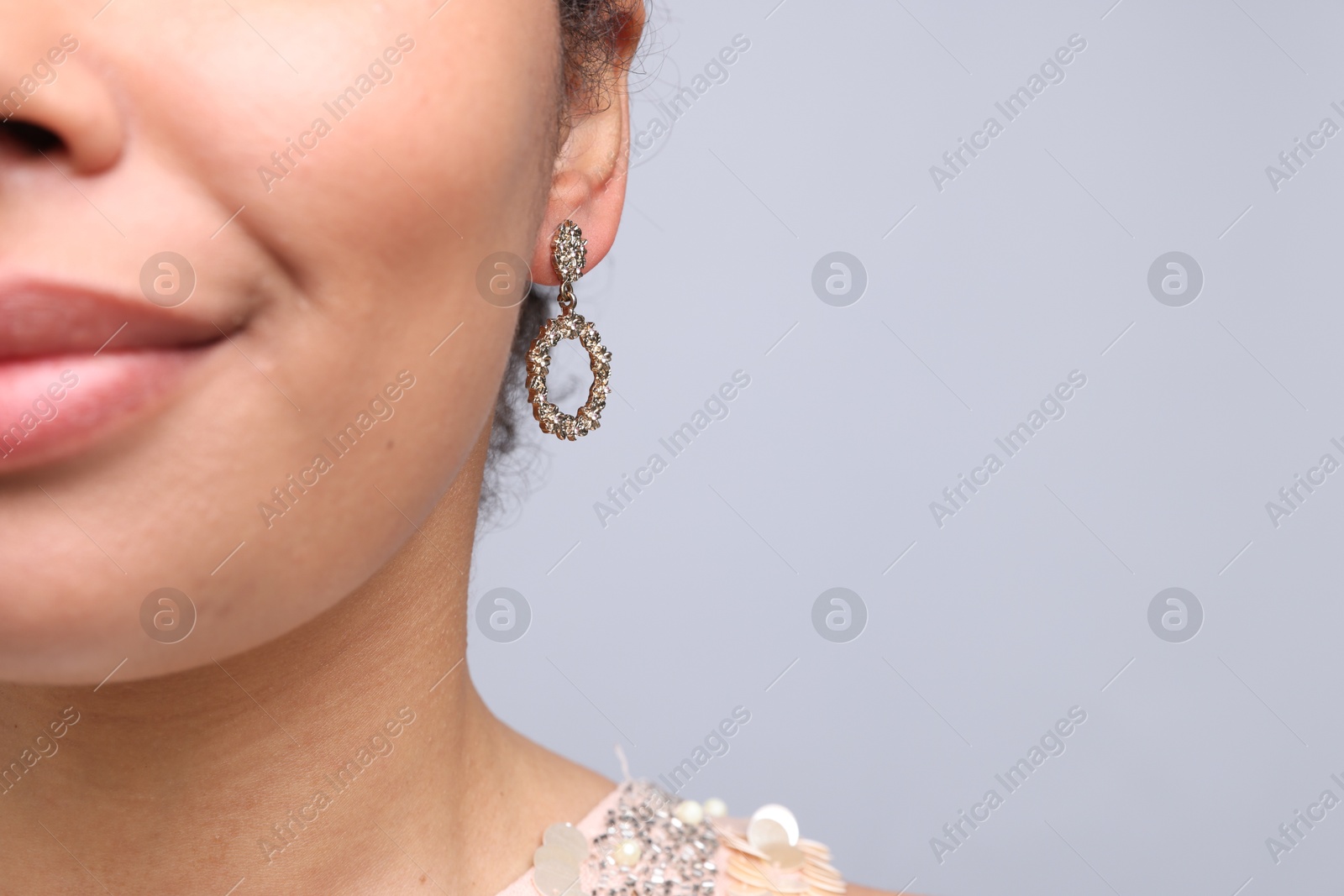 Photo of Young woman wearing elegant earring on light grey background, closeup. Space for text