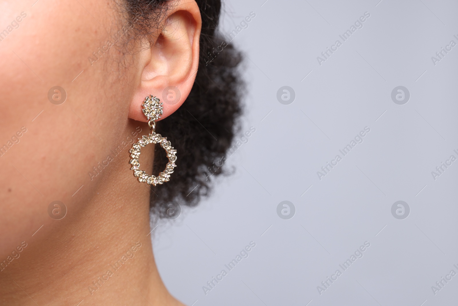 Photo of Young woman wearing elegant earring on light grey background, closeup. Space for text