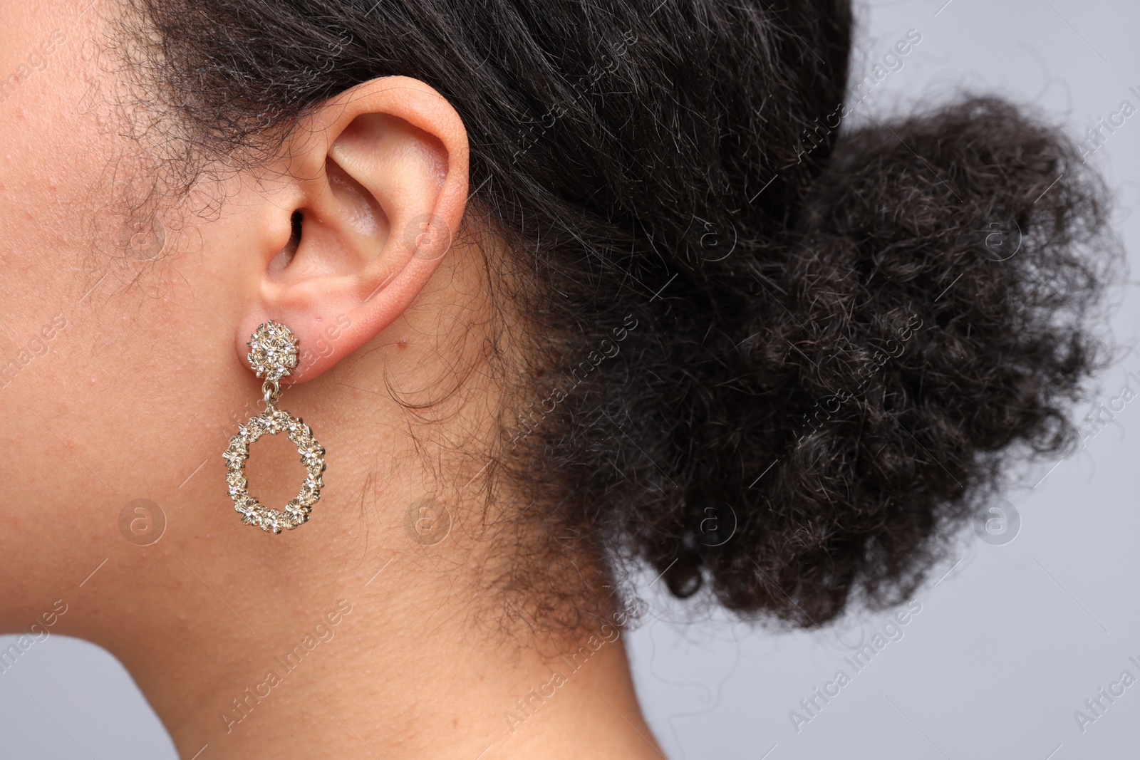 Photo of Young woman wearing elegant earring on light grey background, closeup