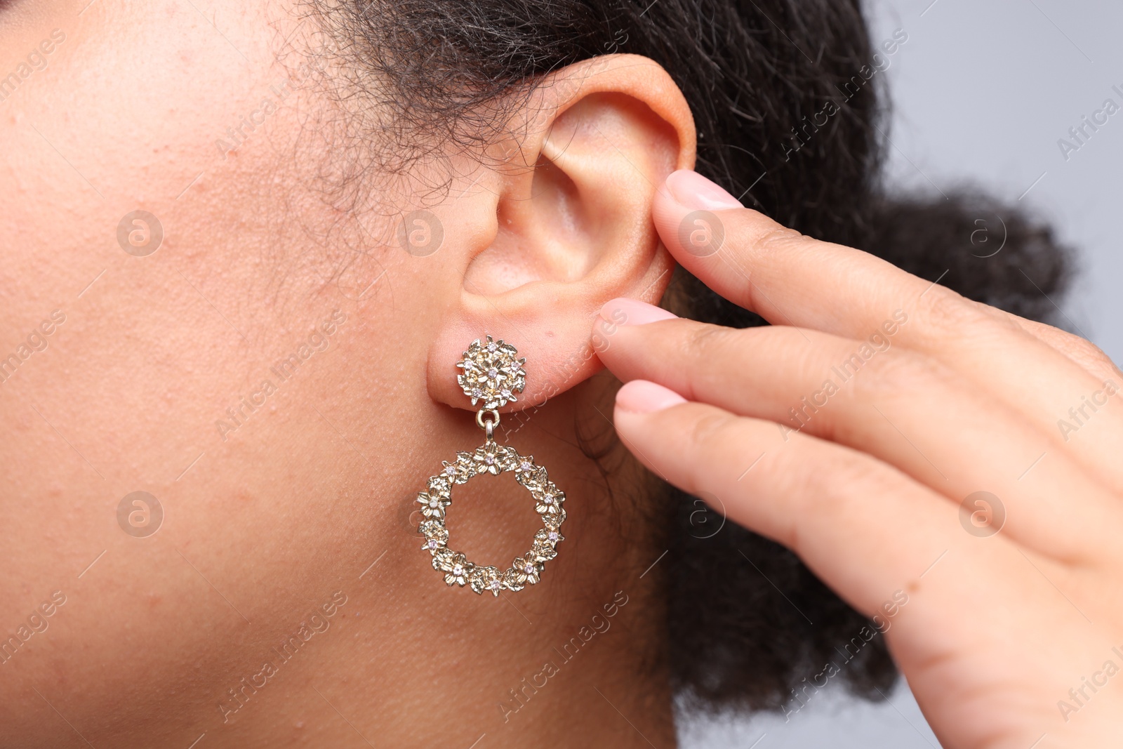 Photo of Young woman wearing elegant earring on light grey background, closeup