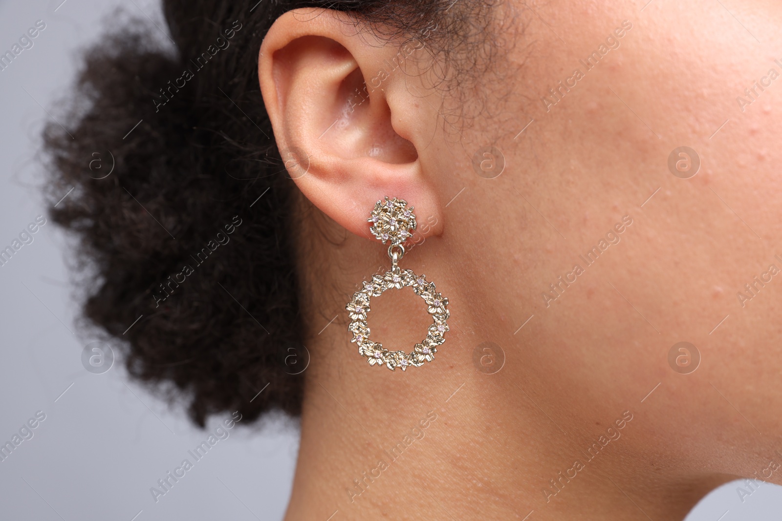 Photo of Young woman wearing elegant earring on light grey background, closeup