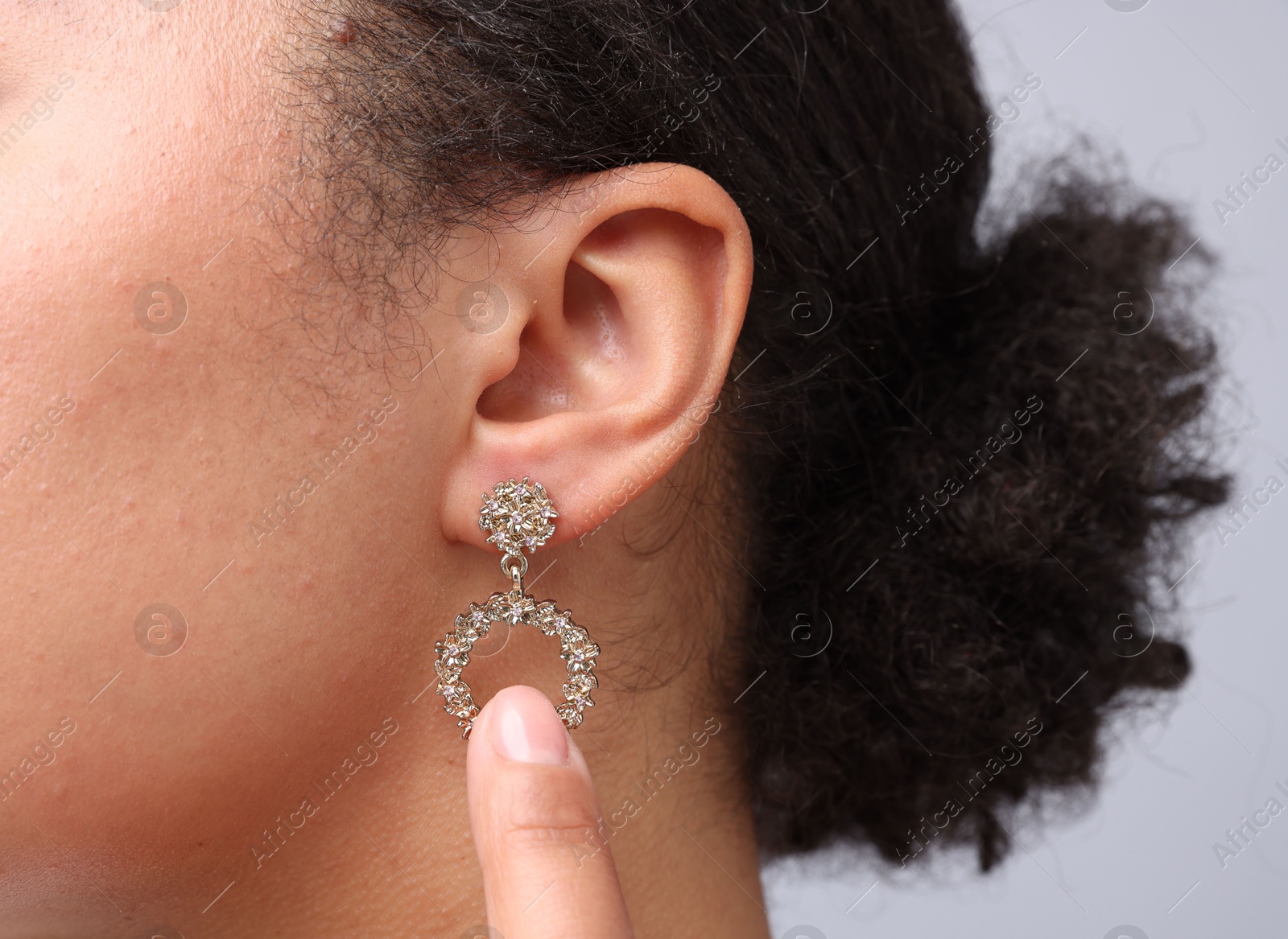 Photo of Young woman wearing elegant earring on light grey background, closeup