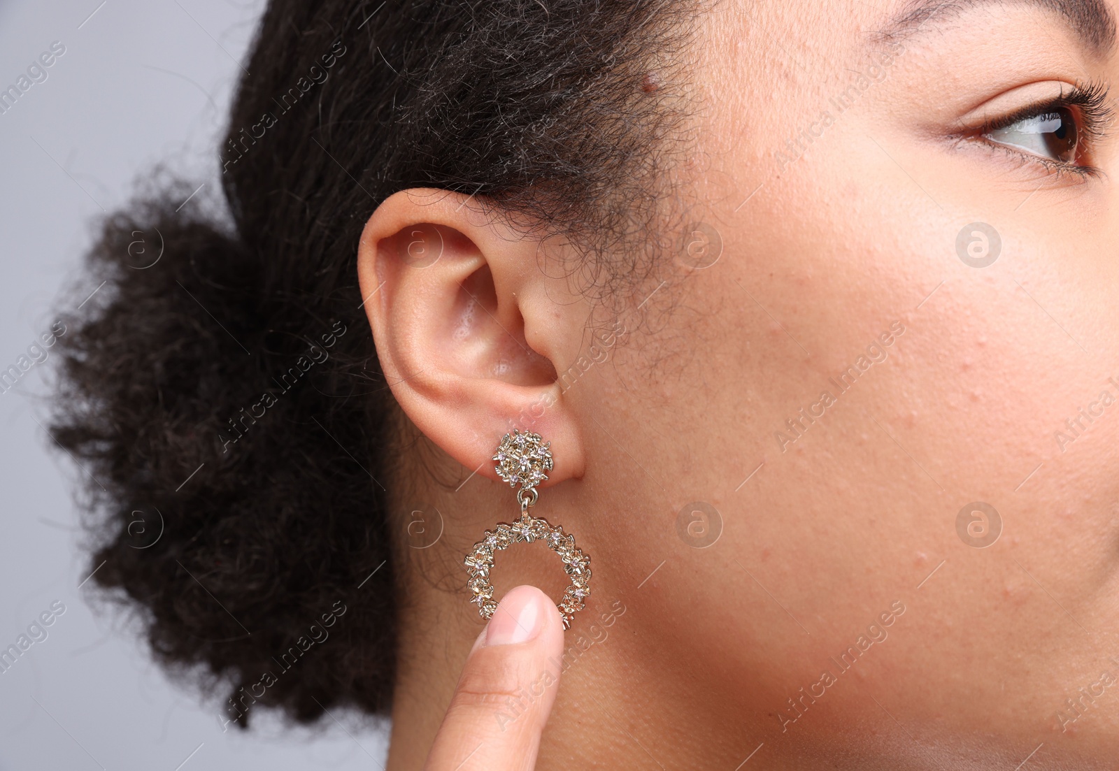 Photo of Young woman wearing elegant earring on light grey background, closeup