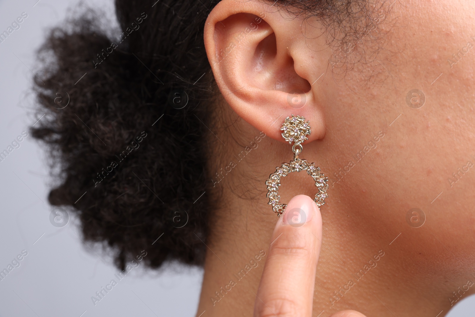 Photo of Young woman wearing elegant earring on light grey background, closeup