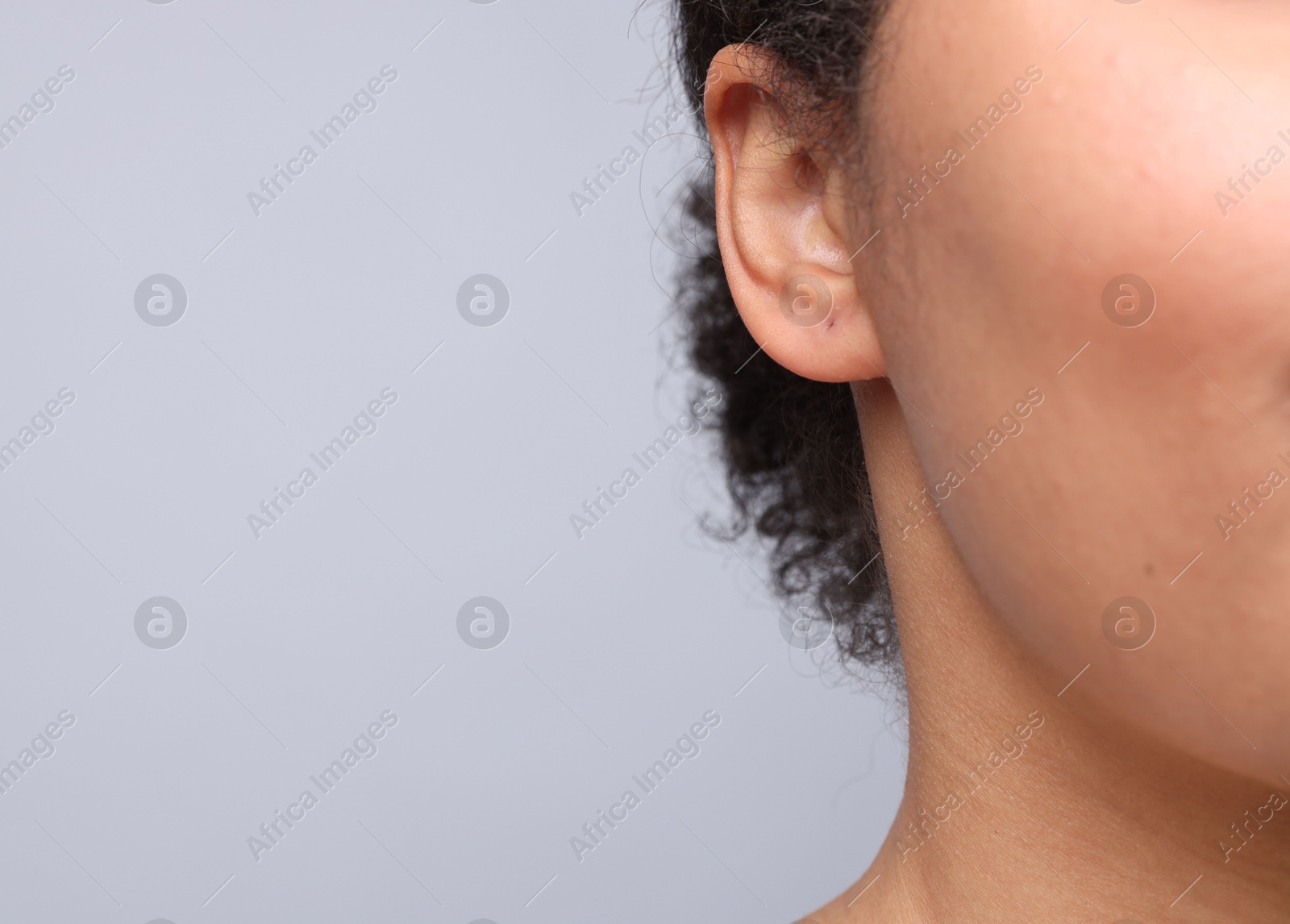 Young woman with pierced ear on light grey background, closeup. Space for text Photo of Young woman with pierced ear on light grey background, closeup. Space for text
