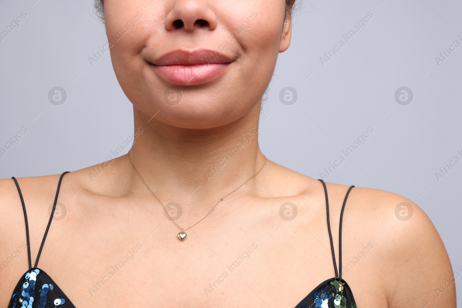 Photo of Young woman wearing elegant gold necklace on light grey background, closeup