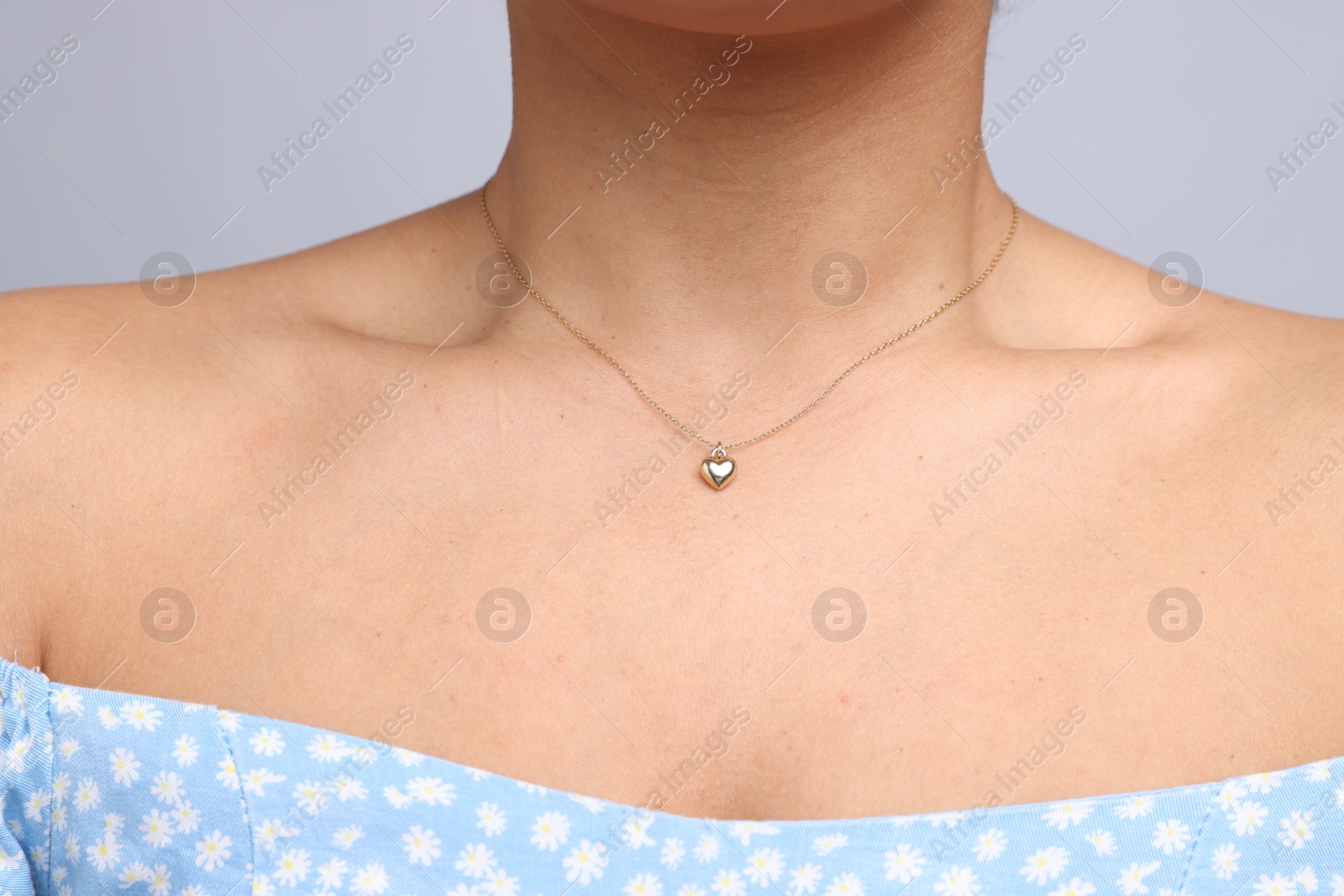 Photo of Young woman wearing elegant gold necklace on light grey background, closeup