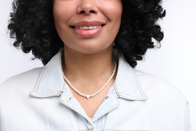 Photo of Young woman wearing elegant pearl necklace on white background, closeup