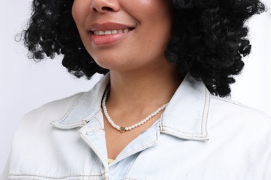 Photo of Young woman wearing elegant pearl necklace on white background, closeup