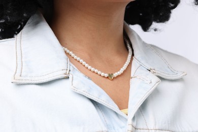 Photo of Young woman wearing elegant pearl necklace on white background, closeup