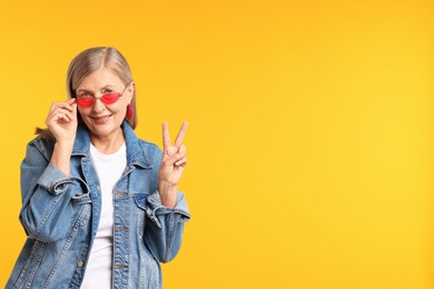 Photo of Senior woman in stylish outfit showing v-sign on orange background, space for text
