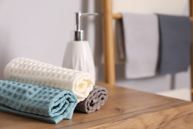 Photo of Clean waffle towels and hand soap on wooden dresser, closeup. Space for text