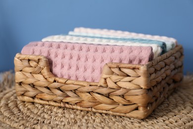 Photo of Clean waffle towels in wicker basket on mat near blue wall, closeup