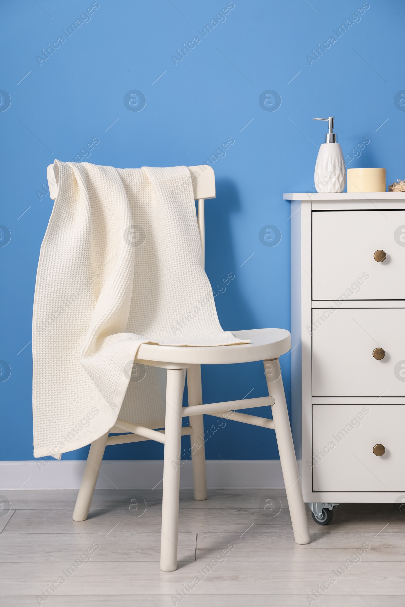 Photo of Clean waffle towel on chair and dresser near blue wall