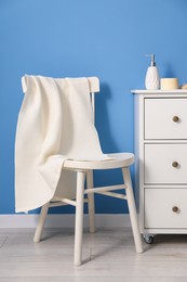 Photo of Clean waffle towel on chair and dresser near blue wall