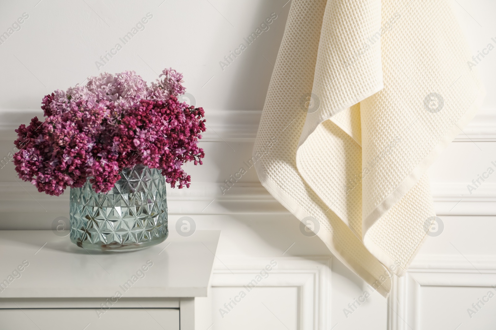 Clean waffle towels and vase of lilac flowers on white dresser in bathroom Photo of Clean waffle towels and vase of lilac flowers on white dresser in bathroom
