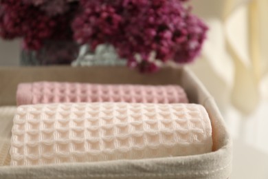 Photo of Clean waffle towels in basket and vase of lilac flowers, closeup