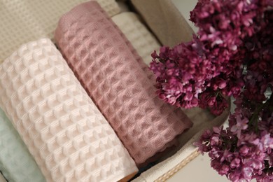 Photo of Clean waffle towels in basket and vase of lilac flowers on white table, top view