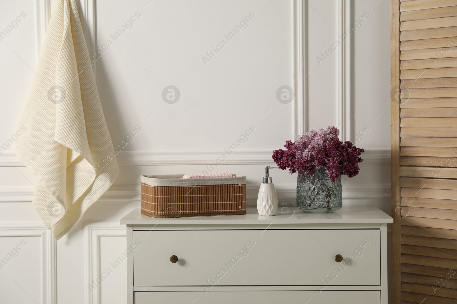 Clean waffle towels and vase of lilac flowers on white dresser in bathroom Photo of Clean waffle towels and vase of lilac flowers on white dresser in bathroom