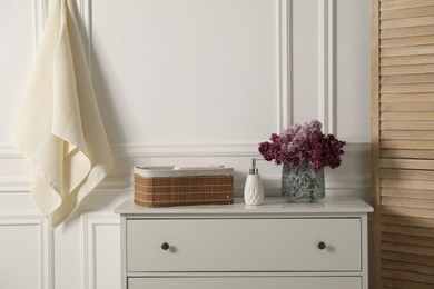 Photo of Clean waffle towels and vase of lilac flowers on white dresser in bathroom