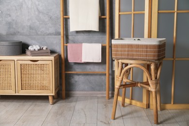 Photo of Clean waffle towels, wooden rack and dresser near grey wall in bathroom