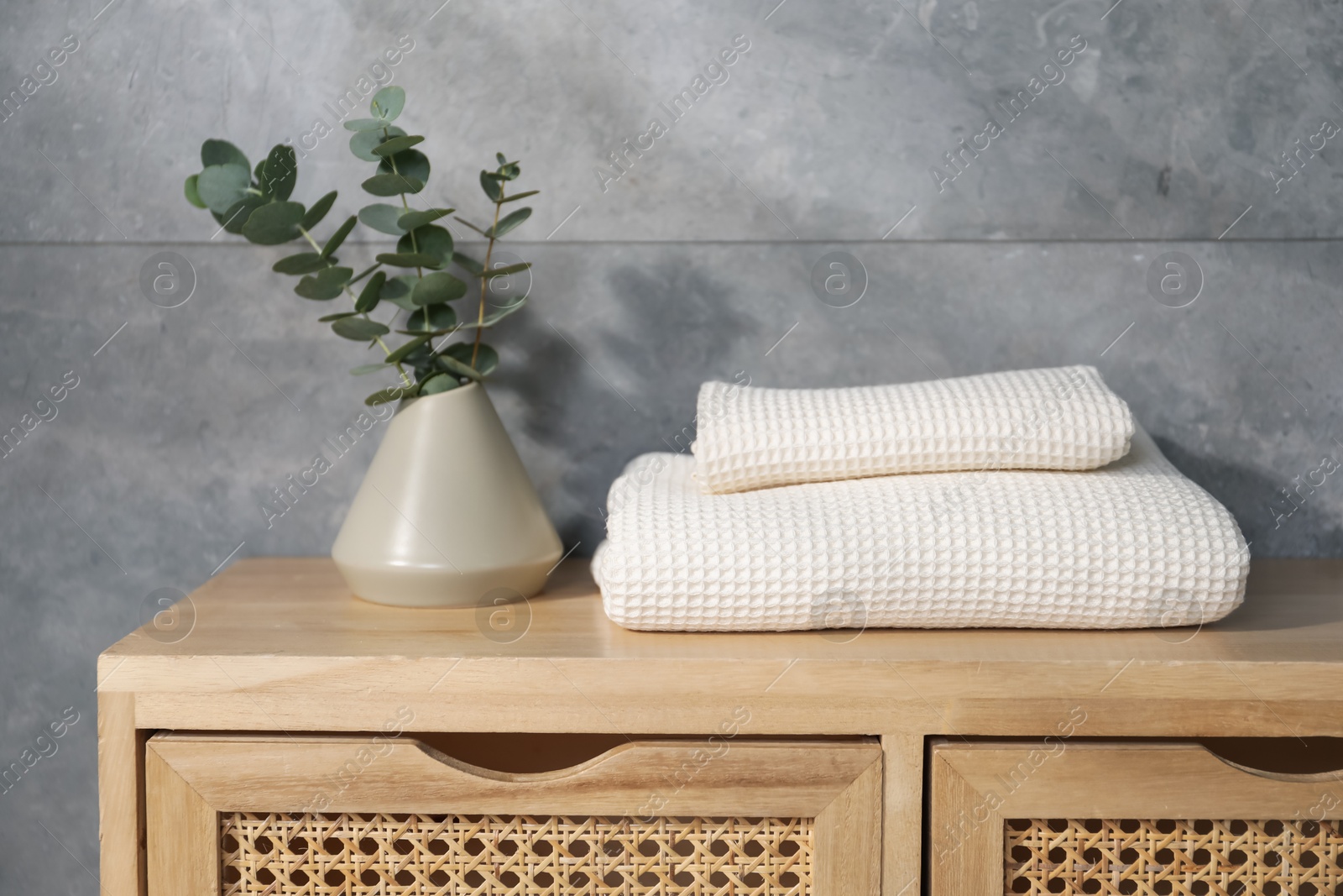 Waffle towels and vase with branches on wooden dresser near grey wall Photo of Waffle towels and vase with branches on wooden dresser near grey wall