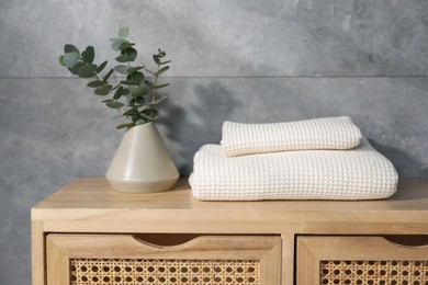 Photo of Waffle towels and vase with branches on wooden dresser near grey wall
