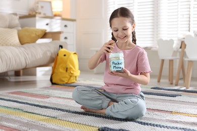 Photo of Girl putting her pocket money into jar at home. Space for text