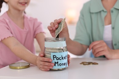 Photo of Mother giving her daughter pocket money at table indoors, closeup