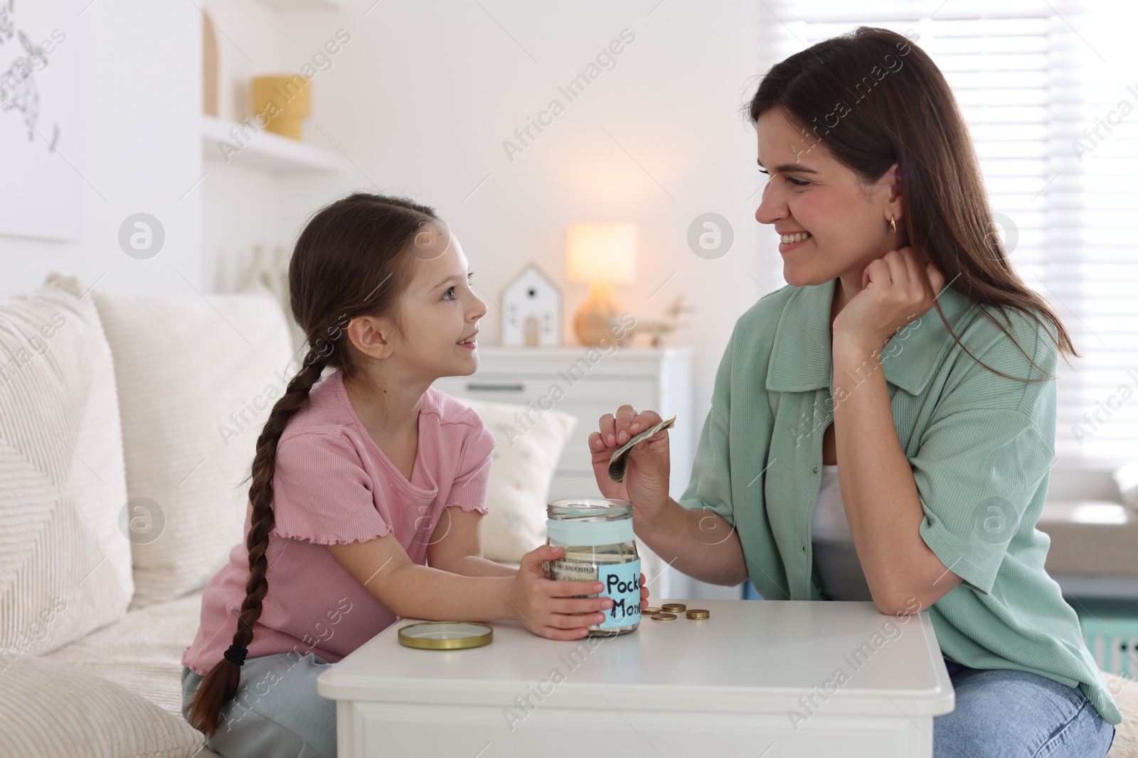 Mother giving her daughter pocket money at table indoors Photo of Mother giving her daughter pocket money at table indoors