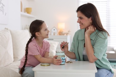 Photo of Mother giving her daughter pocket money at table indoors
