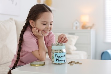 Photo of Girl putting her pocket money into jar at table indoors. Space for text