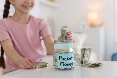 Photo of Girl putting her pocket money into jar at table indoors, closeup. Space for text