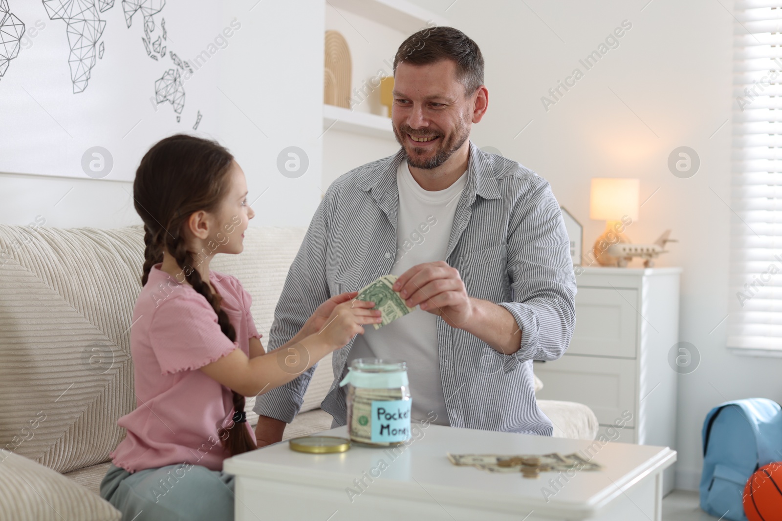 Father giving his daughter pocket money at table indoors Photo of Father giving his daughter pocket money at table indoors