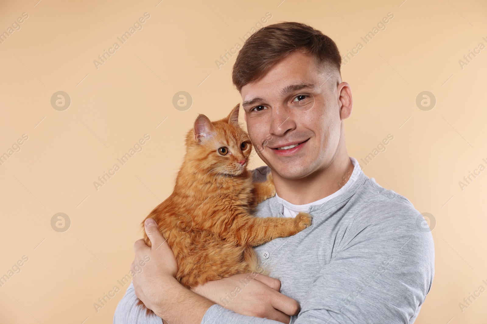 Photo of Man with cute ginger cat on beige background