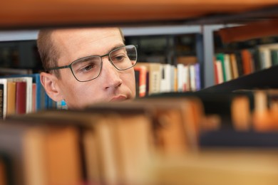Photo of Man choosing book from shelf in public library, closeup