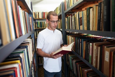 Photo of Man reading book near shelves in public library
